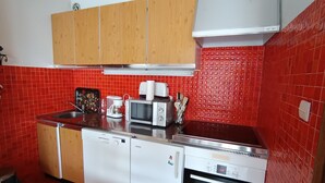 A compact kitchen with red-tiled walls, wooden cabinets, a microwave, a coffee maker, and a dishwasher.
