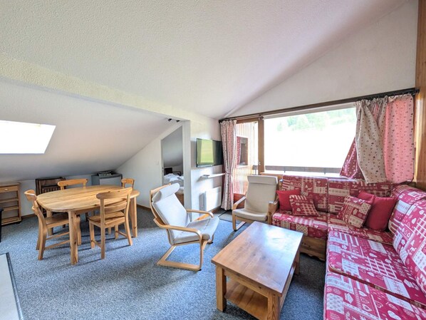 Una sala acogedora con una mesa de comedor de madera, sillas, un sofá y un televisor.