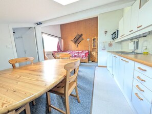 Un comedor con una mesa y sillas de madera, una cocina con armarios blancos y pomos de madera, y una pared de madera.