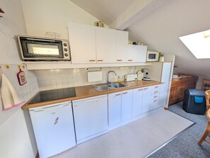 Una cocina compacta con armarios blancos, microondas, lavavajillas y una pequeña encimera.