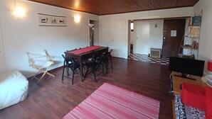 A room with a wooden ceiling, a dining table with chairs, a red rug, a white couch, and a television.