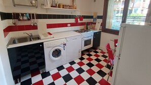 A compact kitchen with a washing machine, a sink, and a window with a view of a balcony.