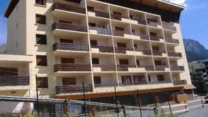 A multi-story hotel with balconies, a flat roof, and a mountainous backdrop.