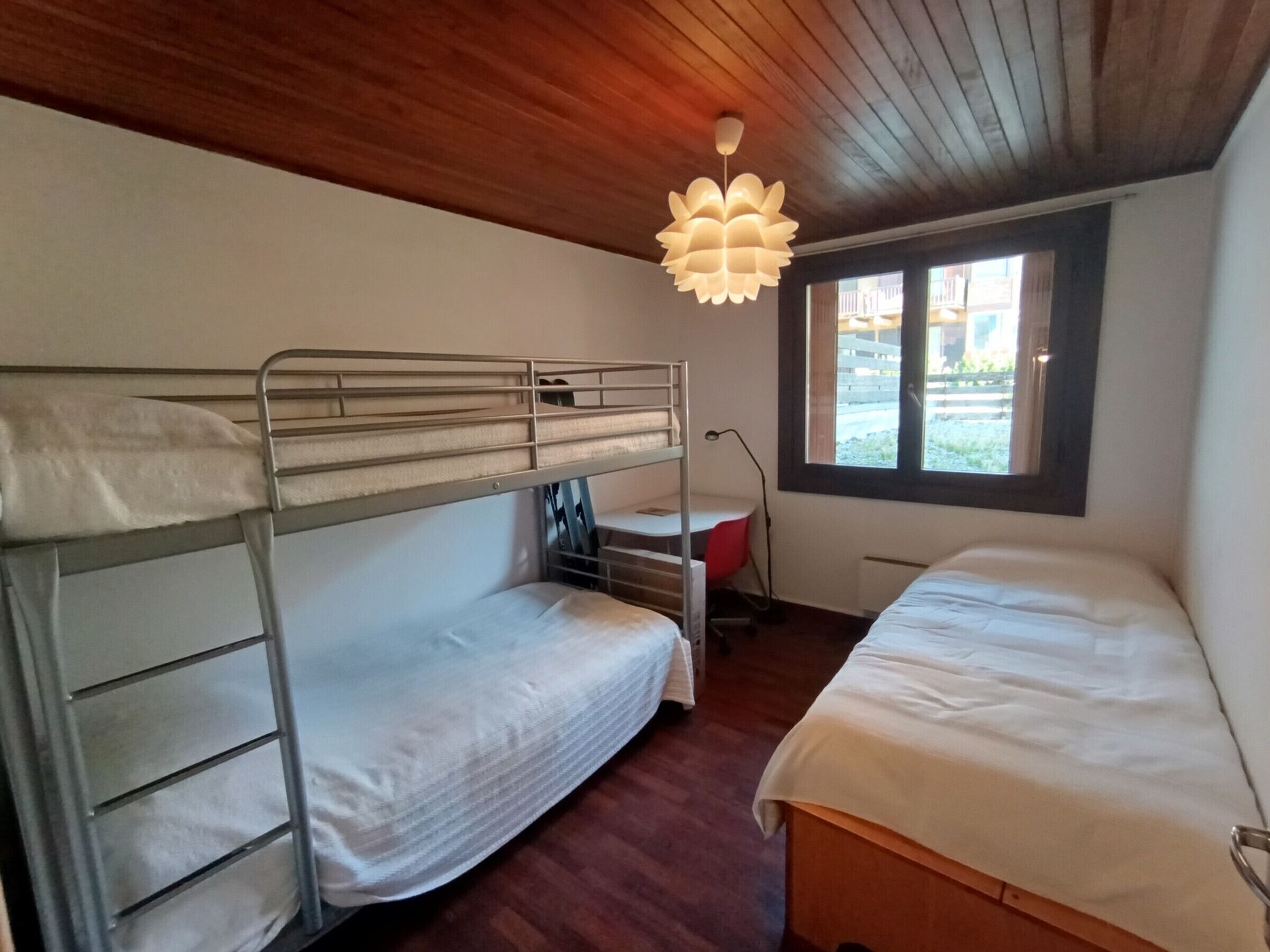 A dormitory room with bunk beds, a desk, and a window with a view of the outside.