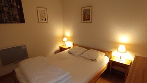 A neatly made bed with white linens and pillows, two bedside lamps, and two framed pictures on the walls. - Ski-in/out apartment for 6, pet friendly, slope views (Montgenèvre)