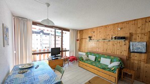 A cozy room with a wooden wall, a sofa, a dining table, a TV, and a window with curtains. - Studio with south-facing balcony, parking in Montgenèvre, pets allowed (Montgenèvre)