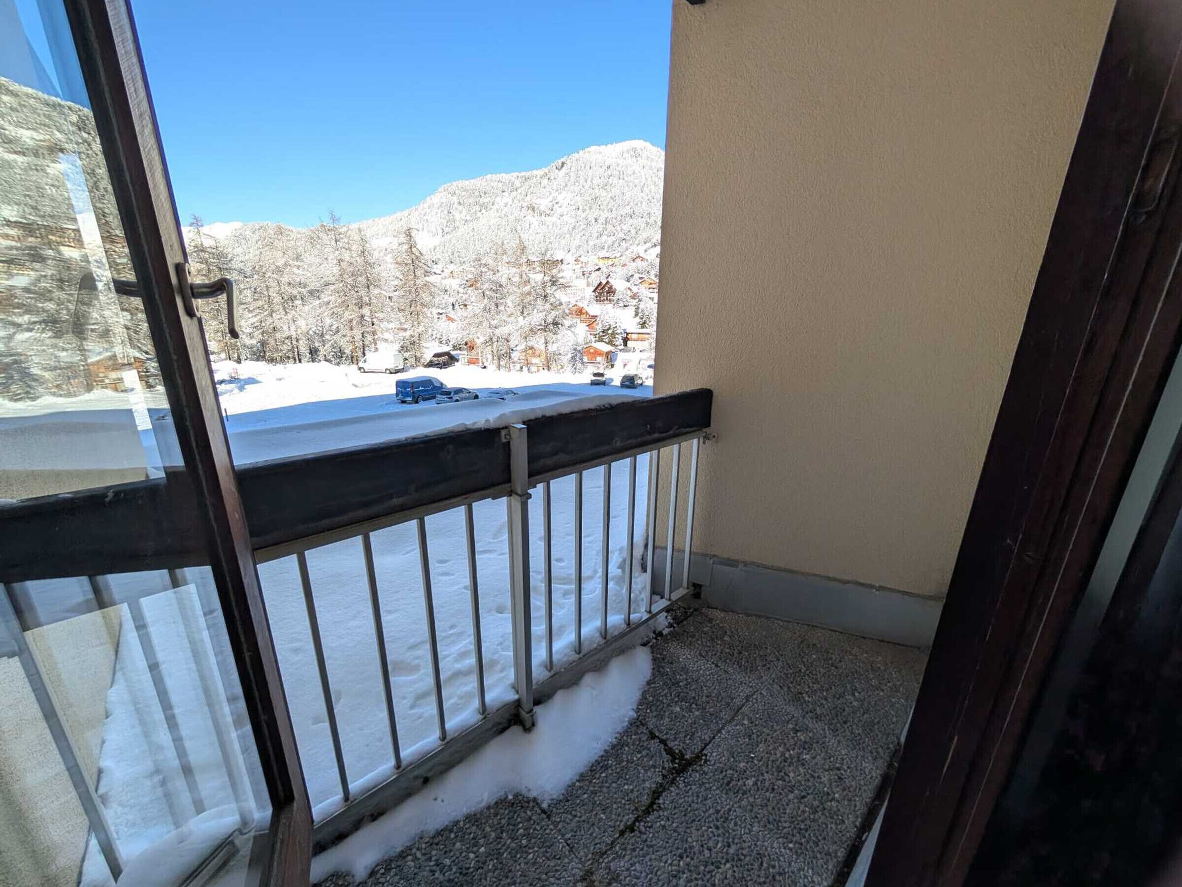 Un balcon avec une balustrade en métal, un paysage enneigé et un ciel bleu dégagé.