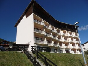 A multi-story hotel with balconies on each floor, a sloped roof, and a staircase leading to the entrance.