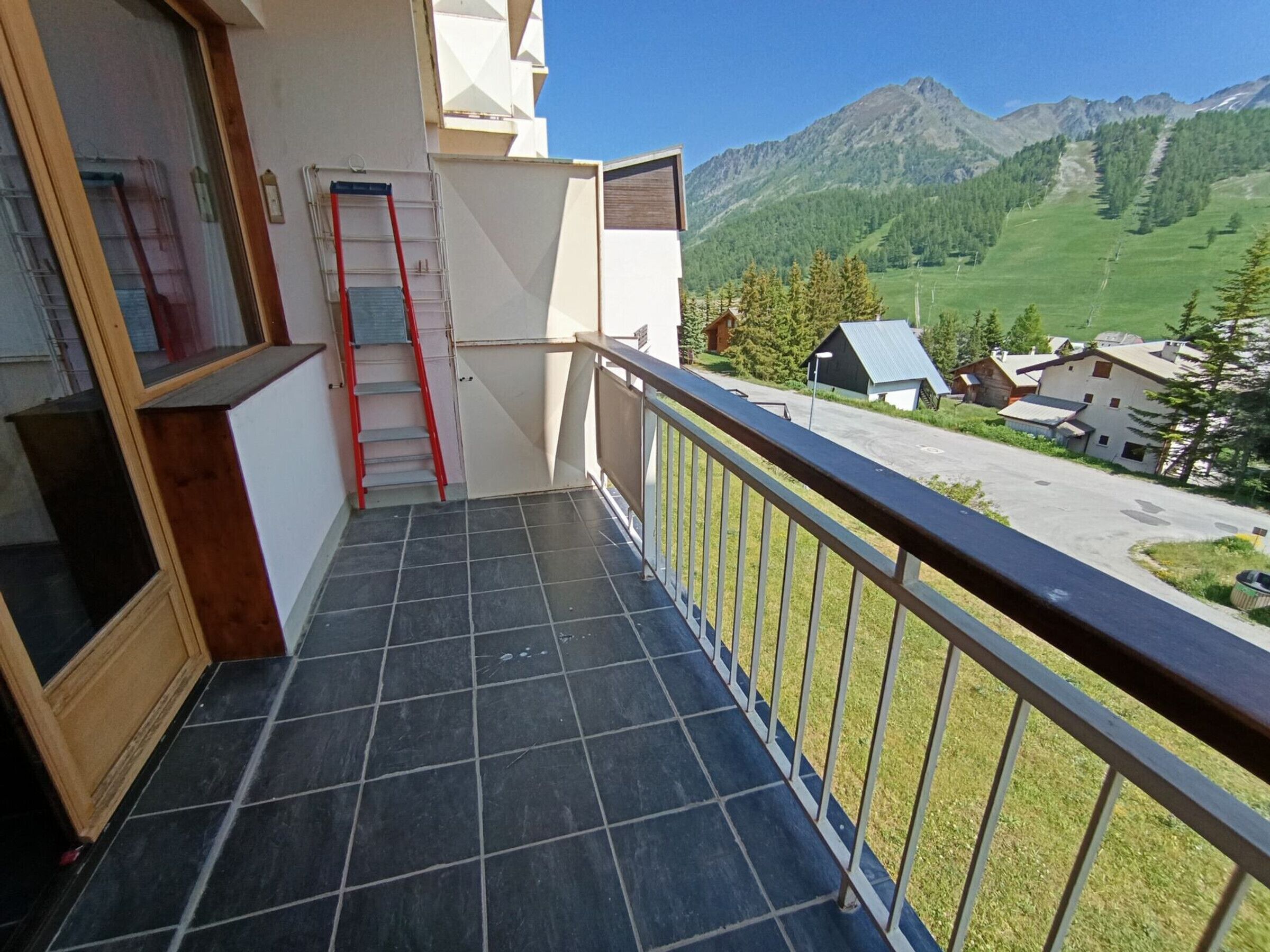 A balcony with a tiled floor, a red ladder, and a railing.