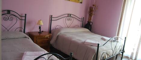 A bedroom with two beds, a nightstand with a lamp, a vase with flowers, and a painting on the wall.