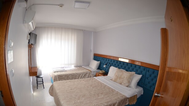 Ein Hotelzimmer mit zwei Betten, einem Holzkopfteil, einem Schreibtisch mit Stuhl und einem Fenster mit Vorhängen.