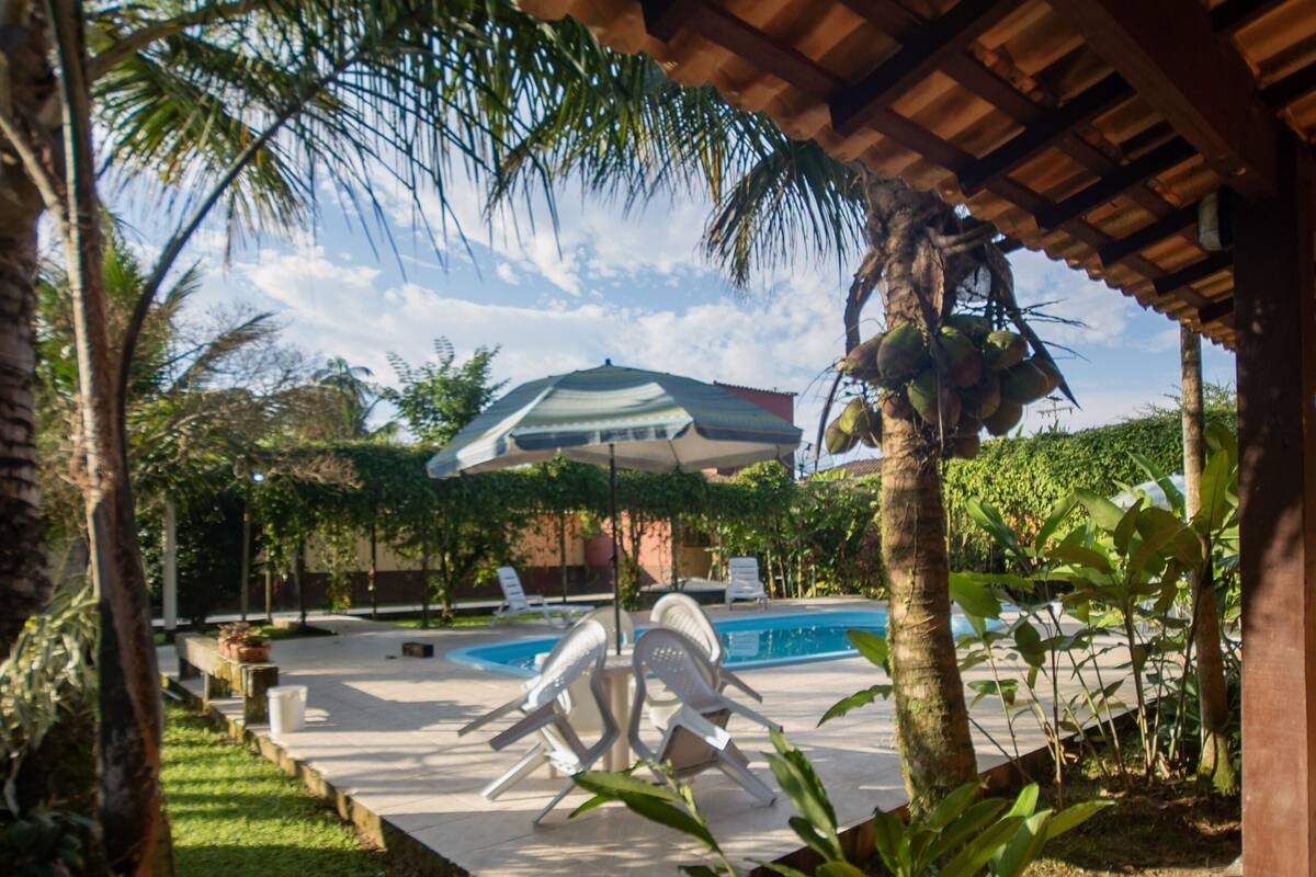 A covered outdoor area with a pool, lounge chairs, and potted plants.