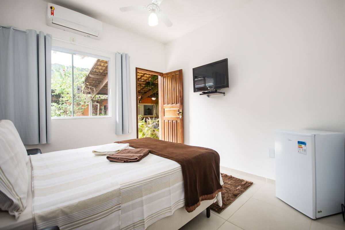 A bedroom with a bed, a television, a refrigerator, and a window with curtains.