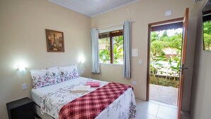 A bedroom with a bed, a nightstand, a window with curtains, and a door leading to a balcony. - Pousada Quatro Estações Paraty (Paraty)