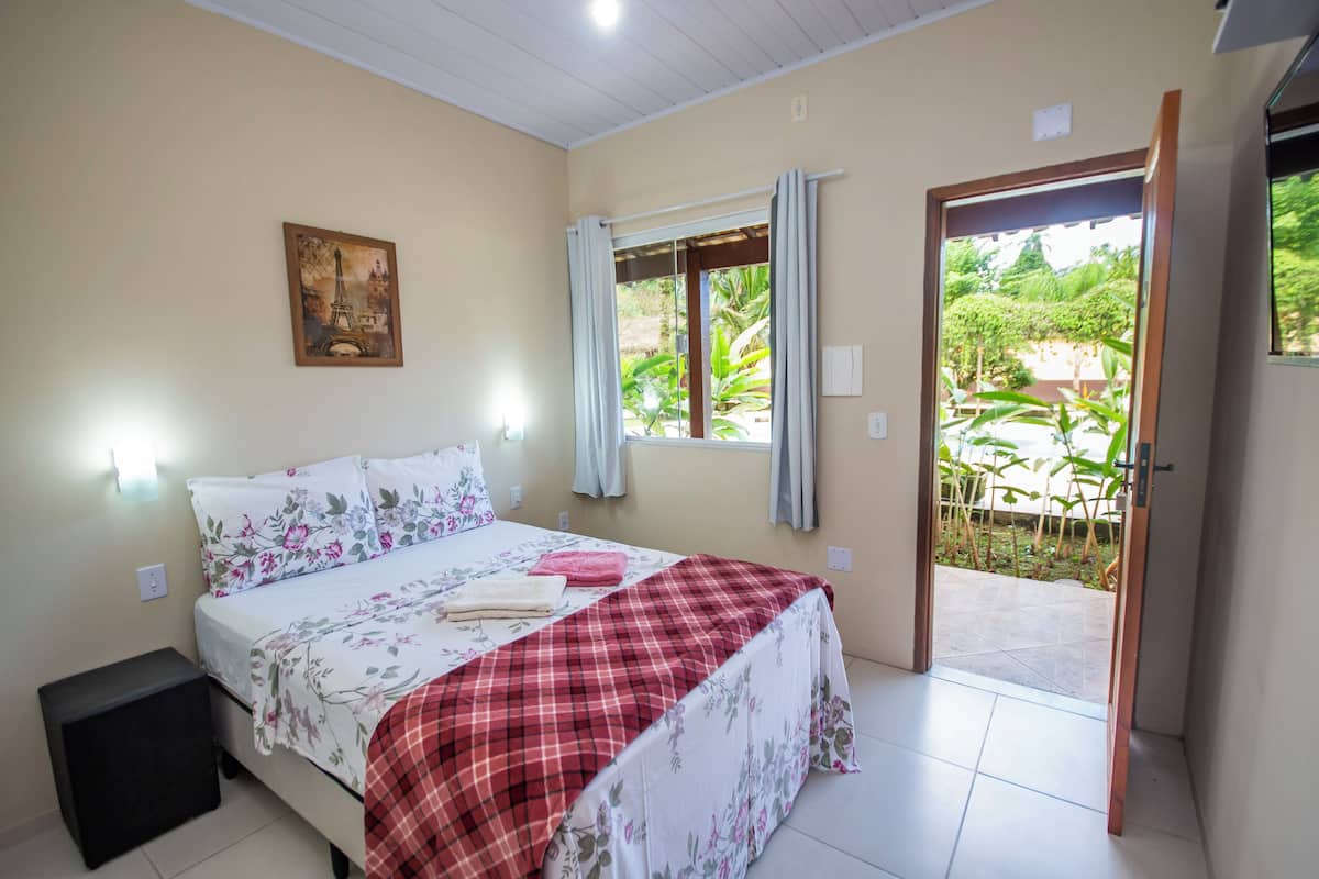 A bedroom with a bed, a nightstand, a window with curtains, and a door leading to a balcony.