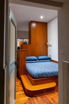 Een kleine slaapkamer met een inbouwslaapbank, houten hoofdbord en een klein nachtkastje.