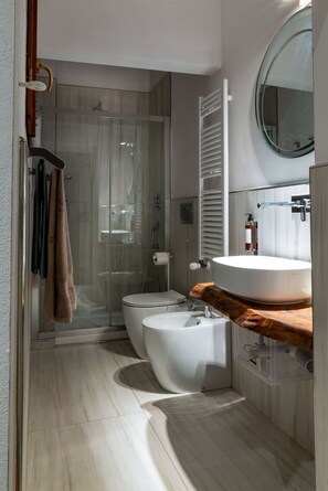 Een moderne badkamer met een douchecabine van glas, twee toiletten, een wastafel met een houten blad en een spiegel boven de wastafel.