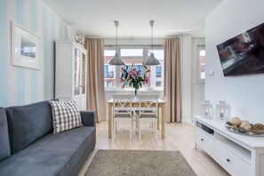 A modern living room with a grey sofa, a dining table with chairs, a TV mounted on the wall, and a window with curtains. - Elite Apartments Center Grobla (Gdansk)