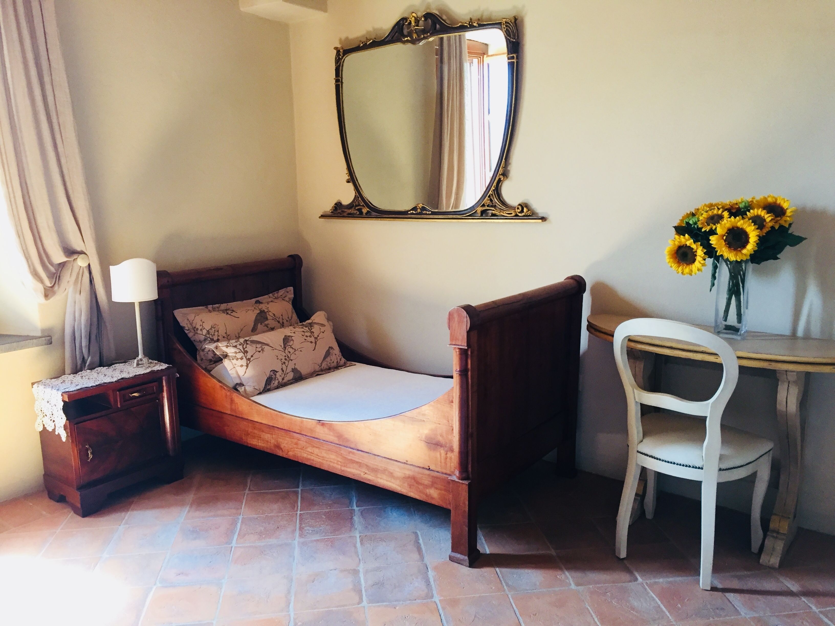 Un dormitorio con una cama de madera, una mesita de noche con lámpara, una silla, un escritorio y un espejo.
