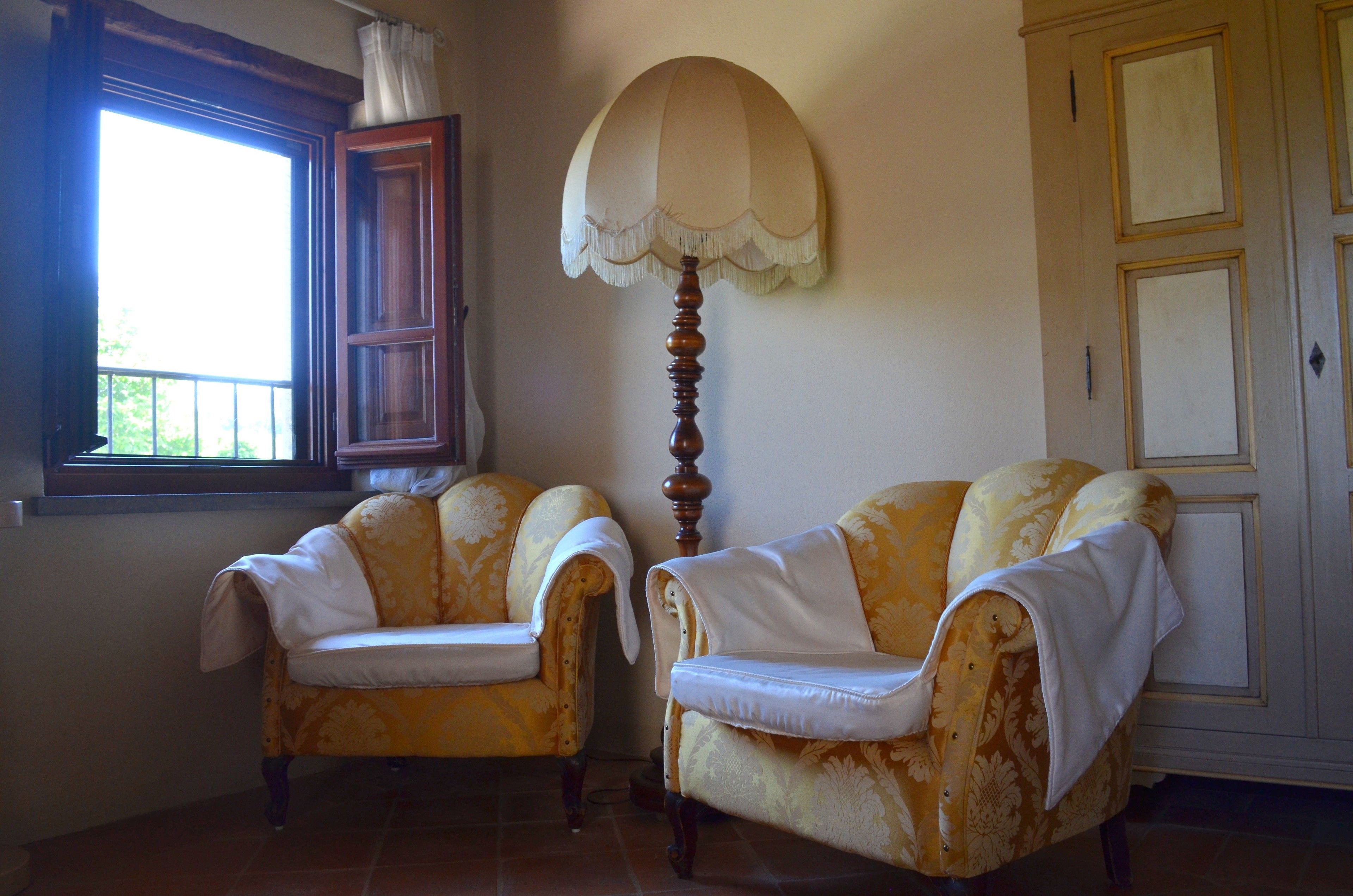Two armchairs with white cushions, a floor lamp, and a window with a curtain.