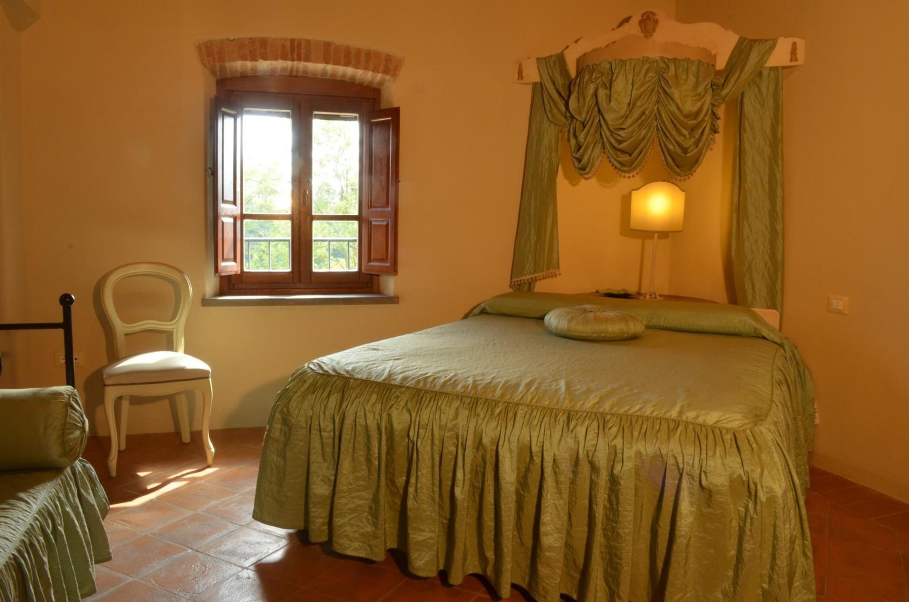 Een slaapkamer met een bed, een stoel, een raam en een lamp.