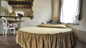 Un dormitorio con cama redonda, una silla blanca, un escritorio, un espejo y una ventana con cortinas.