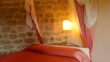 A room with a stone wall, a bed with a red blanket, and a bedside lamp.