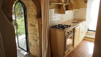 Una cocina con estufa a gas, horno y lavabo, una ventana con vistas a zonas verdes, y una puerta que da al exterior.