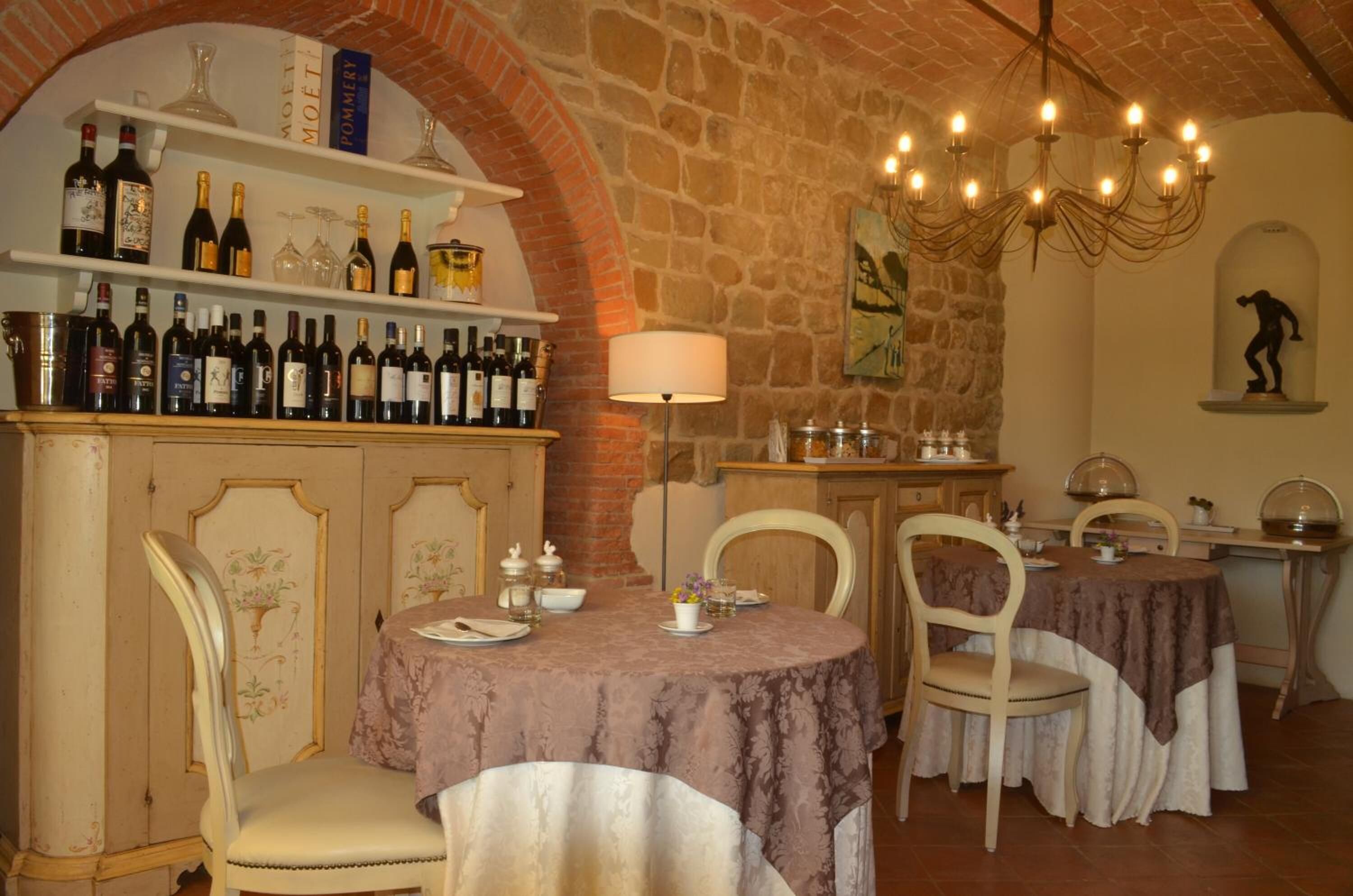 Un restaurante con pared de piedra, una estantería para vinos y dos mesas con sillas.