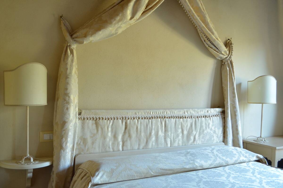 A bedroom with a canopy bed, bedside lamps, and a bedside table.