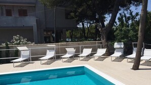 A swimming pool with white lounge chairs arranged along the edge. - La Villa della Meda (Taranto)