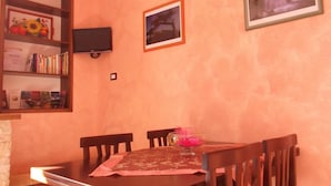 A dining area with a wooden table, four chairs, a television mounted on the wall, and a bookshelf filled with books and decorative items. - Dolcedorme B&B (Terranova di Pollino)