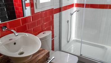 Baño con lavamanos blanco, inodoro y ducha con mampara de vidrio.