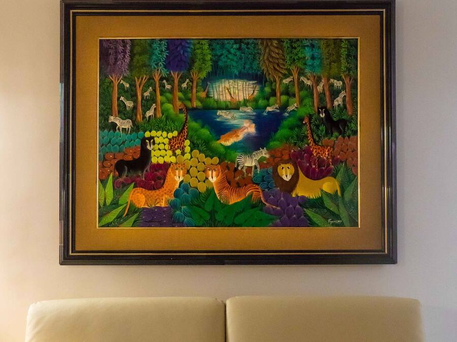 Un tableau encadré représentant une scène de la nature, placé au-dessus d’un canapé beige agrémenté d’un coussin à rayures colorées.