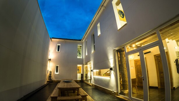 A narrow courtyard with a wooden bench, a statue, and a building entrance with glass doors.