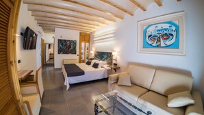 A hotel room with a bed, a sofa, a glass coffee table, and artwork on the walls.