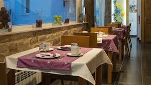 A restaurant with wooden beams, stone pillars, and a long counter with a view. Tables are set with white tablecloths and purple napkins.