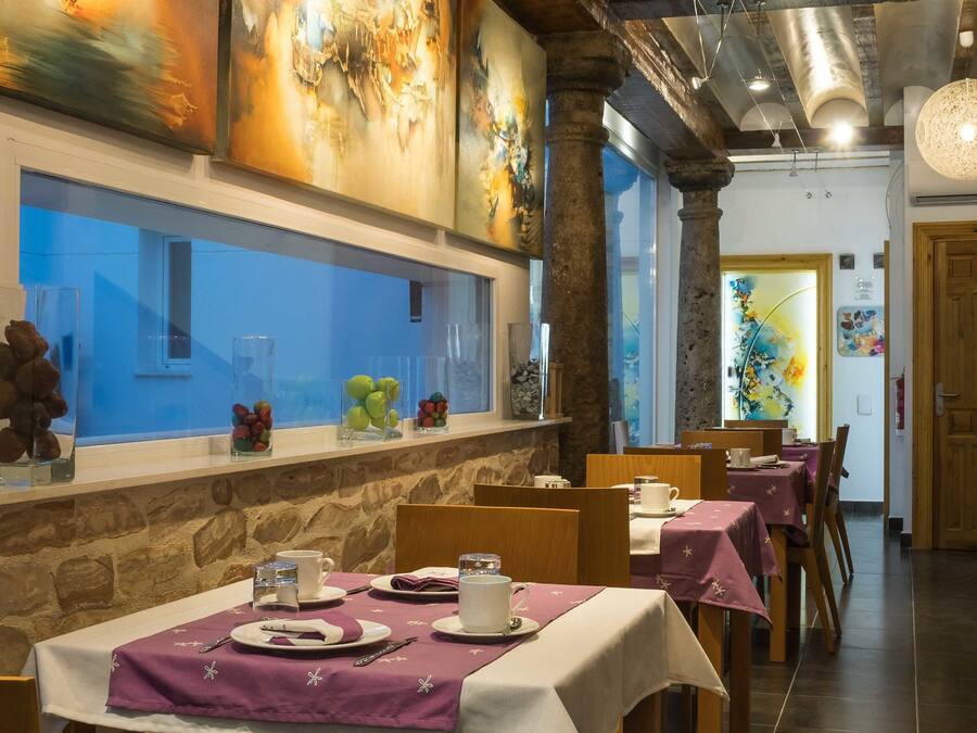 Un ristorante con travi in legno, pilastri in pietra e un lungo bancone con vista. I tavoli sono apparecchiati con tovaglie bianche e tovaglioli viola.