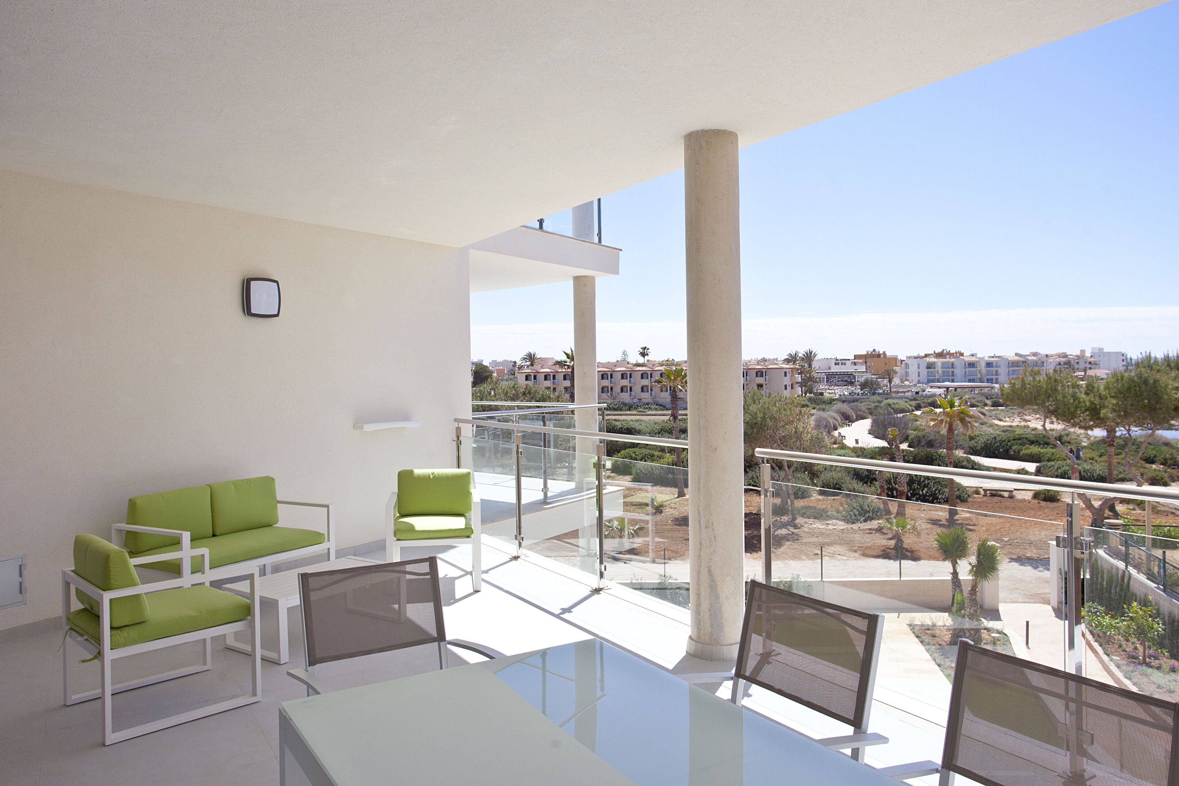A balcony with a glass railing, a white table, and green chairs.