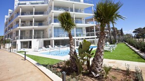 Un hotel de varios pisos con piscina, asientos al aire libre y palmeras.