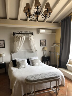 A bedroom with a four-poster bed, a standing lamp, a bedside table, and a window with curtains. - Entre vignes et dentelles (Courthezon)