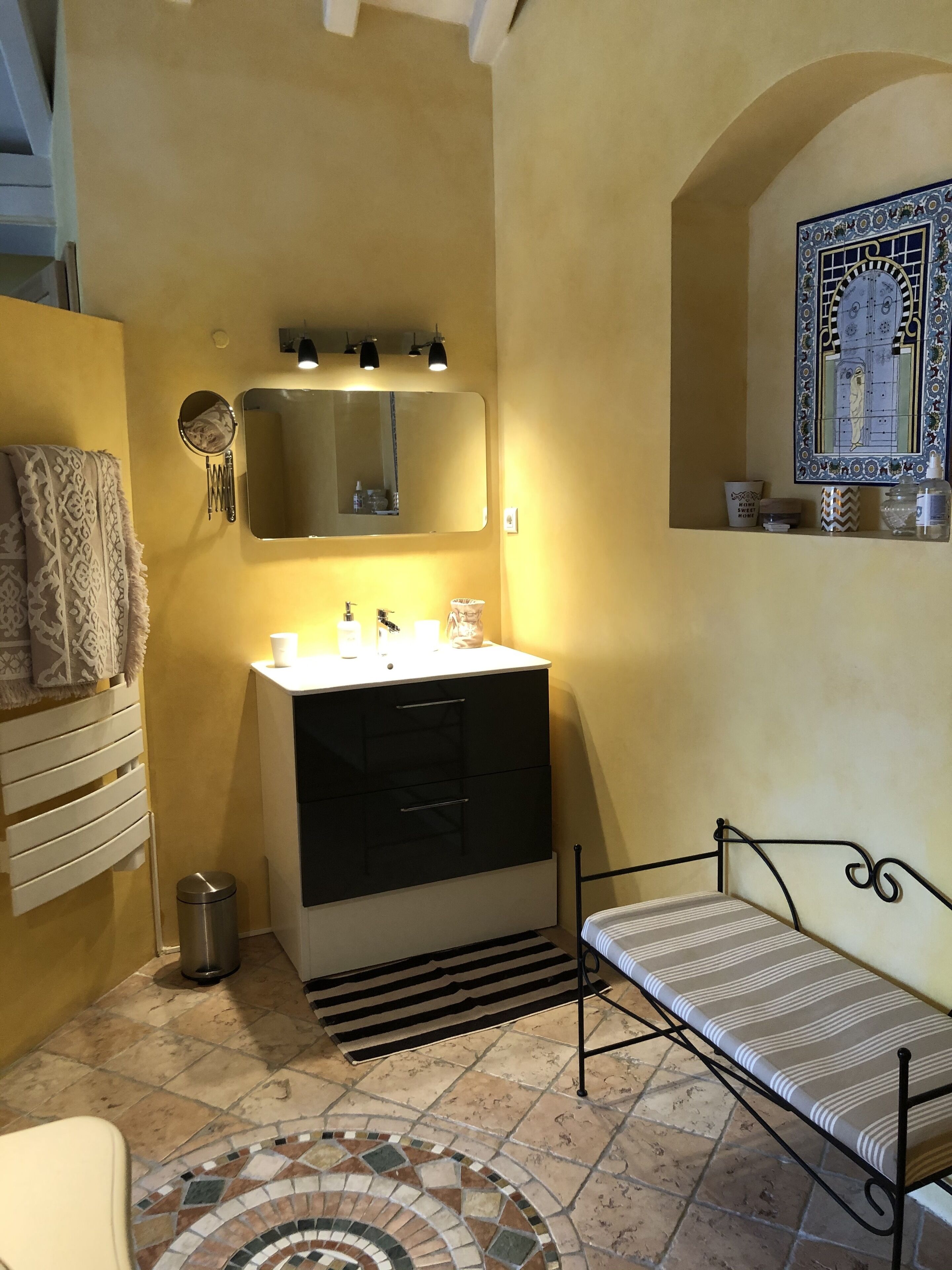A bathroom with a sink, mirror, and a small window with decorative tiles.