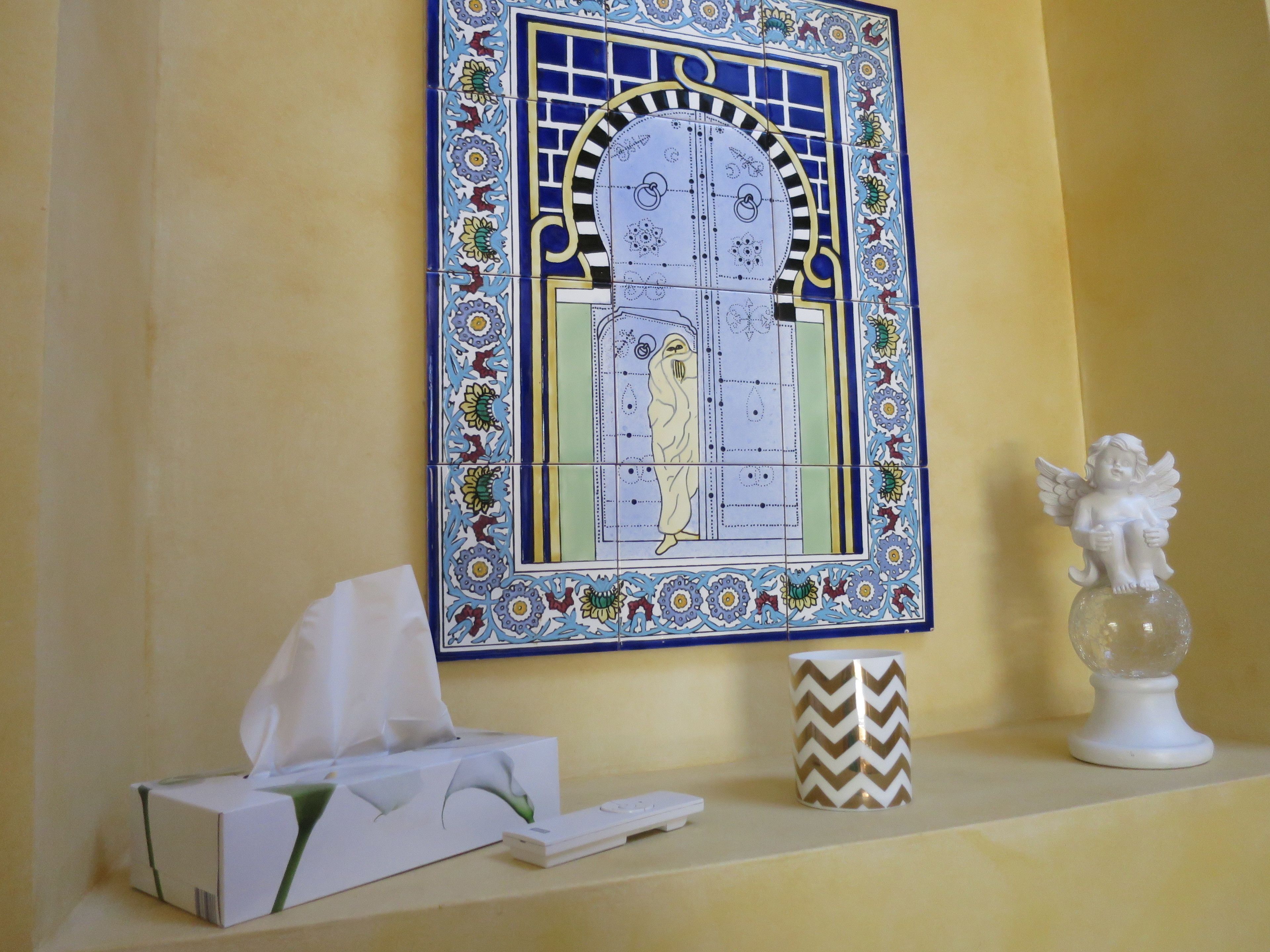 A tiled wall with a decorative pattern, a tissue box, a remote control, and a small angel figurine on a shelf.