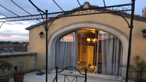 A rooftop terrace with a wrought iron bed, potted plants, and a view of a building with an arched entrance.