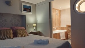 A hotel room with a bed, a nightstand, a lamp, a framed picture, and a view of the bathroom.