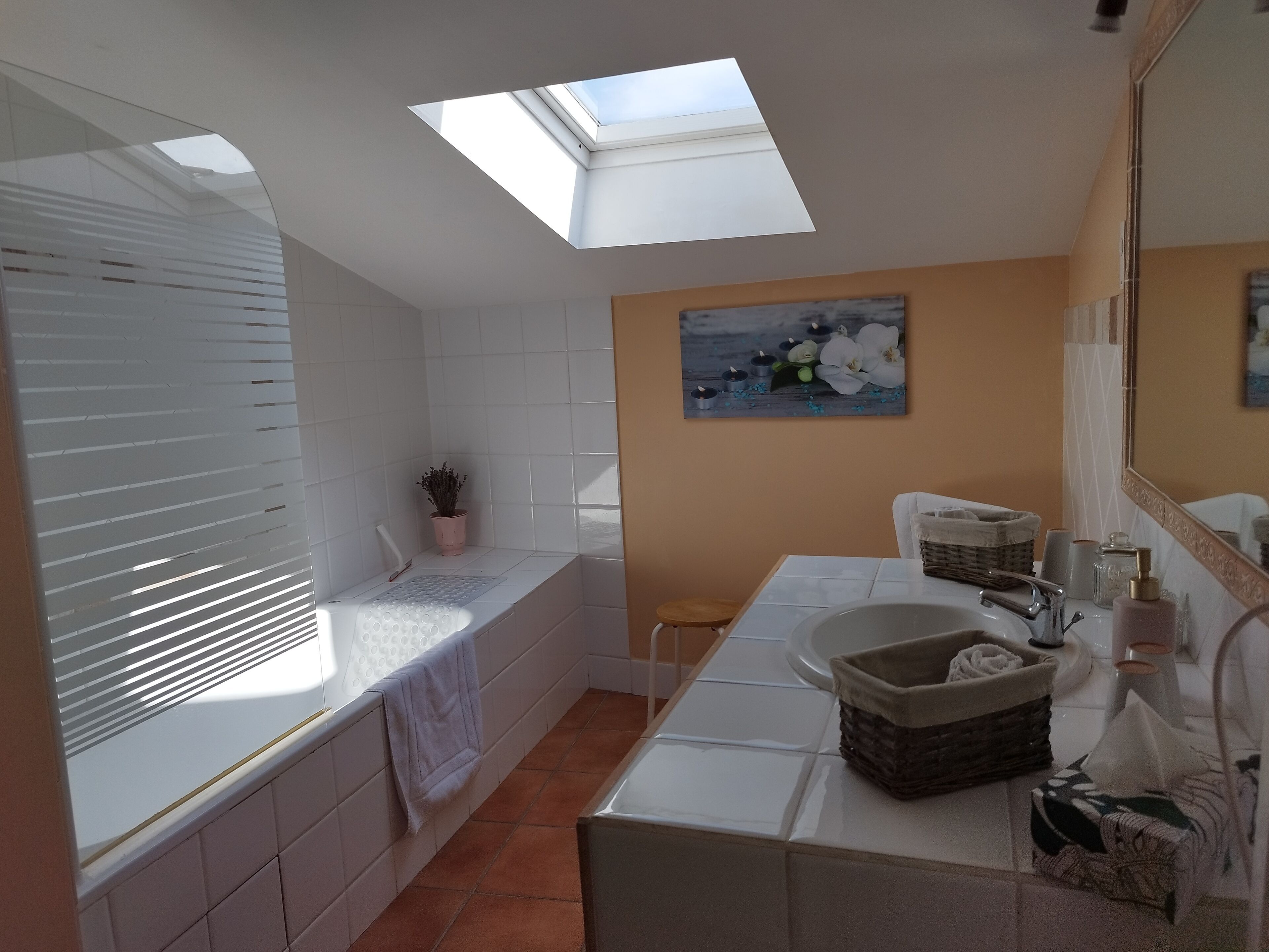 A bathroom with a skylight, a bathtub, a sink, and a mirror.
