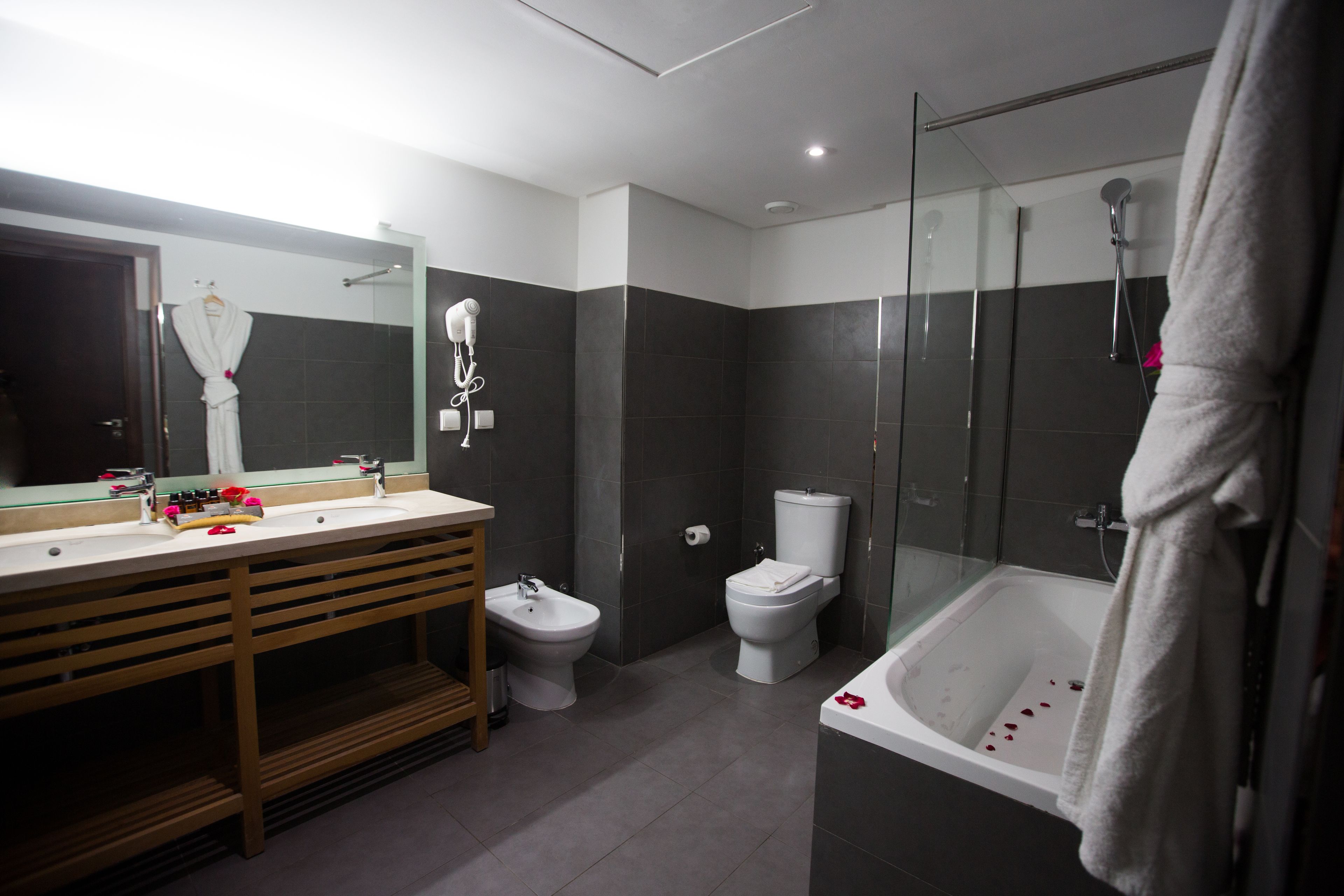 A modern bathroom with a large mirror, a vanity with a sink, a bidet, a toilet, and a bathtub.