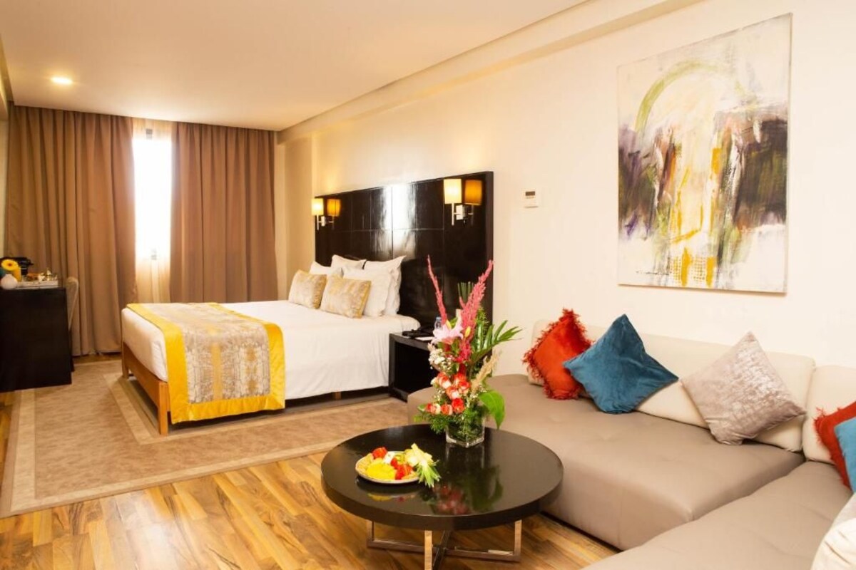 A hotel room with two beds, a sofa, a coffee table, and a painting on the wall.