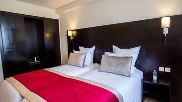 A hotel room with a large bed, two bedside tables, a red blanket, and a water bottle on one of the tables.