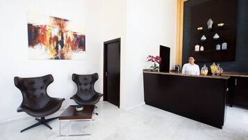 Un espace d’accueil au design moderne, comprenant deux fauteuils en cuir noir, un comptoir d’accueil en bois et un grand tableau abstrait accroché au mur.
